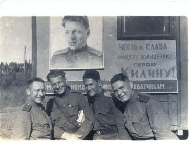 Майор Килин с боевыми товарищами на фоне плаката со своим портретом.