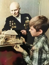 Николай Гаврилович показывает макет родного дома собственного изготовления внуку Михаилу